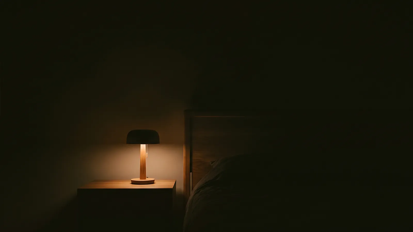 불 꺼진 침실, 스탠드 하나만 켜진 원목 침대 머리맡